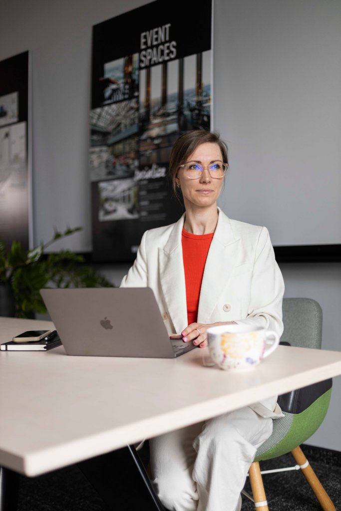 Freiberufliche Projektmanagerin bei der Arbeit. Janine sitzt am Schreibtisch. Vor ihr der Laptop. Sie schaut nach rechts.
